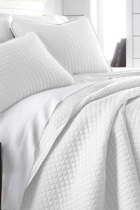 “Bright white oversized quilt bedding set on a queen bed with two matching pillow shams, pet-friendly and wrinkle-resistant.”