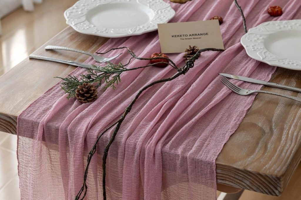 Dusty rose cheesecloth gauze table runner styled on a rustic wooden wedding table