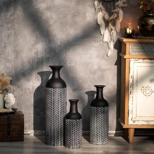 Set of 3 black tall metal floor vases (27/20/16 inches) placed near a modern fireplace.
