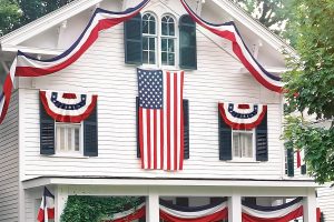 "Large American patriotic bunting flag in red, white, and blue stripes displayed on an outdoor porch railing for 4th of July"