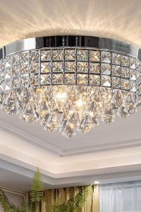 4-light chrome crystal chandelier with round metal shade installed in a dining room