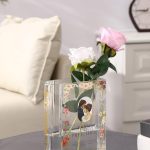 Clear glass book-shaped vase filled with colorful flowers, placed on a wooden table.