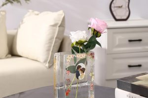 Clear glass book-shaped vase filled with colorful flowers, placed on a wooden table.