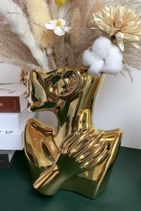Gold ceramic face vase shaped like a human bust, used as a modern decorative flower pot.