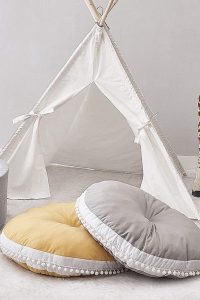 "Large grey round kids floor cushion placed in a nursery reading nook with teepee canopy"