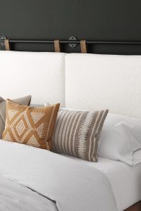 Wall-mounted queen headboard in soft white boucle with brown faux leather hanging straps, modern and minimalist bedroom design by Nathan James
