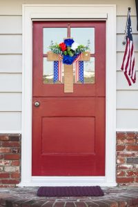 "Rustic wooden cross door decoration with red, white, and blue ribbons and flowers for patriotic holidays like 4th of July and Memorial Day"