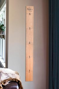 "Natural wooden growth chart for kids with black numerals and 'Love Grows Here' design mounted on a children's room wall"